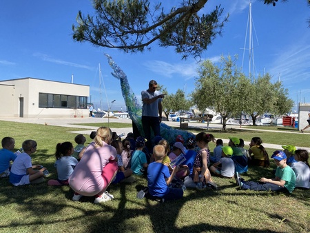 V ospredju so otroci, v ozadju je kit iz odpadnih plastenk, vmes pa Jure Orel.